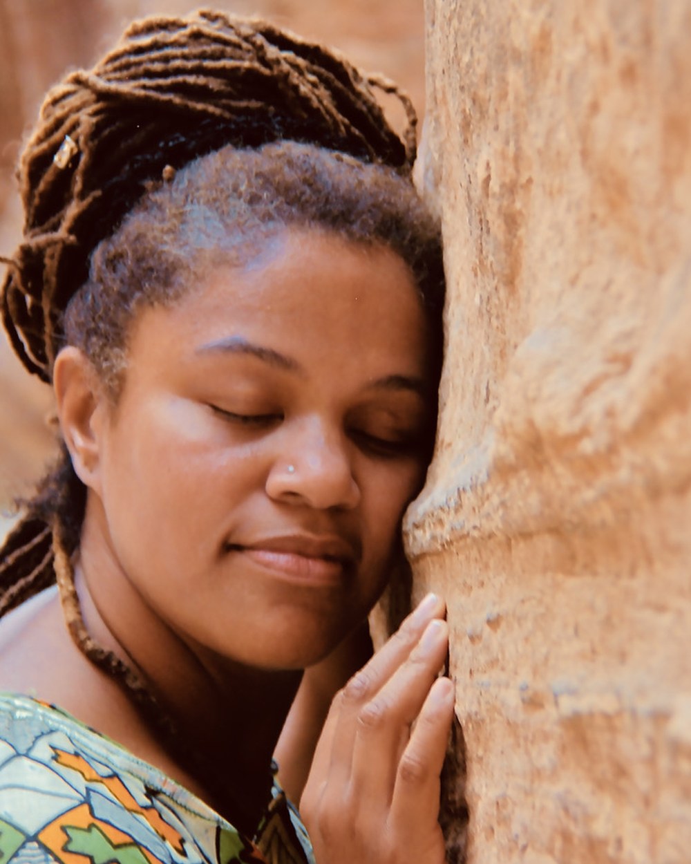 Amikaeyla Gaston, eyes closed, cheek resting against warm stone wall